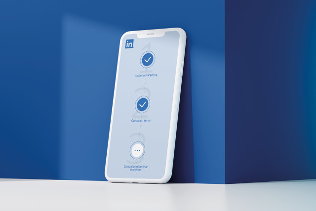 A smartphone leaning against a blue wall, displaying LinkedIn's campaign setup steps on its screen.