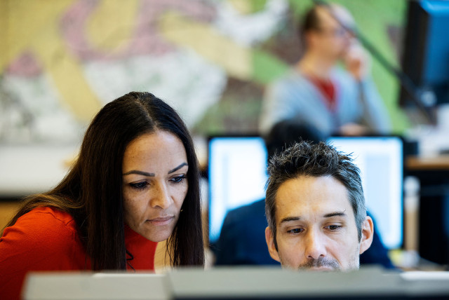 A woman and a man engaged in a focused discussion while working on a computer, symbolizing teamwork and strategic planning in social selling. The background features office monitors, representing a digital and data-driven work environment. | CBC | Cross-Border Communications | Leading international B2B branding and marketing agency
